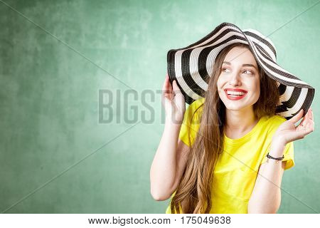 Colorful portrait of a beautiful woman in yellow t-shirt and striped hat on the green background