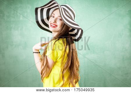 Colorful portrait of a beautiful woman in yellow t-shirt and striped hat on the green background