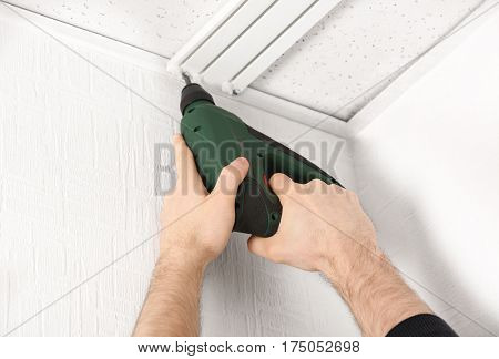 Male hands installing curtain rail using electric screwdriver