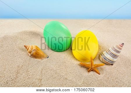 Easter eggs with seashells on sand at shore