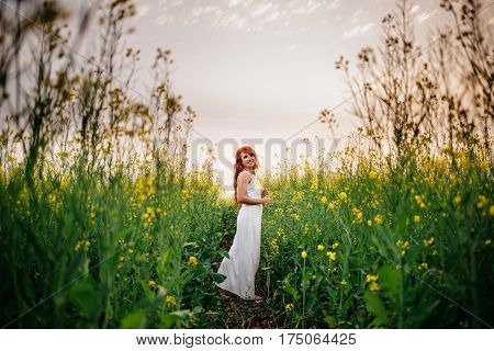 Young beautiful red-haired woman in a blooming rapeseed field at sunset