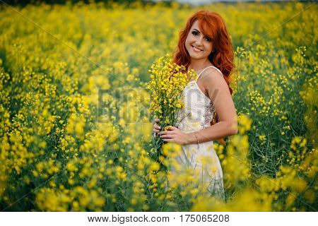 Young beautiful red-haired woman in a blooming rapeseed field at sunset