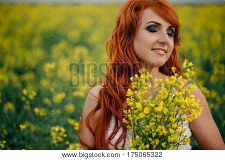 Young beautiful red-haired woman in a blooming rapeseed field at sunset