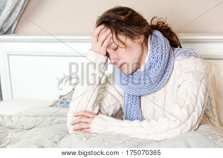 Flu or cold. Closeup top view image of frustrated young woman with blue scarf and suffering from terrible headache while lying in bed.