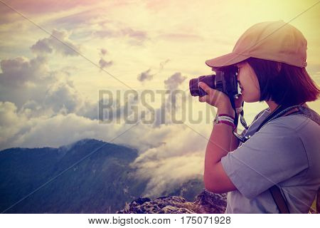 Vintage style hiker asian teens girl with digital camera taking photo beautiful landscape natural of sierra and sky during sunset on mountain at Phu Chi Fa Forest Park Chiang Rai Thailand