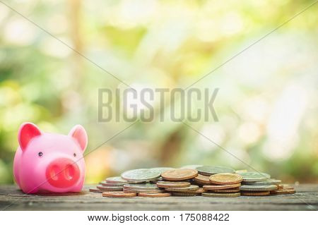 Pink piggy bank and many coins on wooden table for saving concept