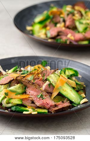 Vertical view of 2 plates of asian beef salad. Inspired by Thai and Vietnamese salads packed with fresh healthy vegetables (carrots onions cucumber etc) and a nicely seared flank steak.