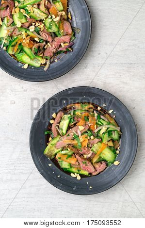 Thai beef salad top view. Two plates of asian beef salad viewed from above, this dish is inspired by Thai & Vietnamese cuisine. This salad is made with fresh healthy vegetables (carrots onions cucumber etc) and a nicely seared flank steak.
