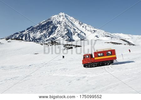 KORYAK VOLCANO KAMCHATKA PENINSULA RUSSIA - APRIL 26 2014: Snowcat driving with sportsman on board (skiers and snowboarders) on snowy slopes of mountains on background of active Koryak Volcano.