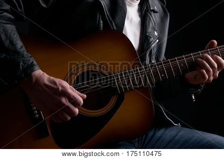 Rockstar in biker leather jacket playing solo on acoustic guitar.