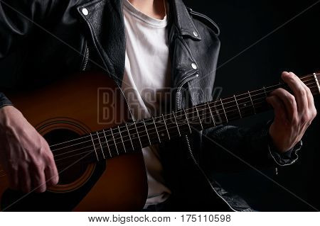 Rockstar in biker leather jacket playing solo on acoustic guitar.