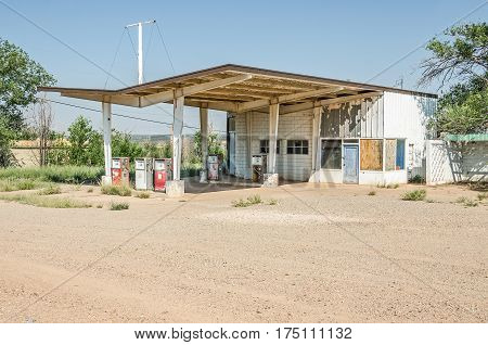 Deserted gas station on Route 66 with windows either broken or boarded up featuring faded and weathered gas pumps