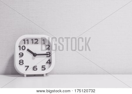 Closeup white clock for decorate show a quarter past ten or 10:15 a.m. on white wood desk and cream wallpaper textured background in black and white tone with copy space