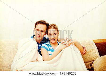 Smiling loving couple sitting on couch with blanket