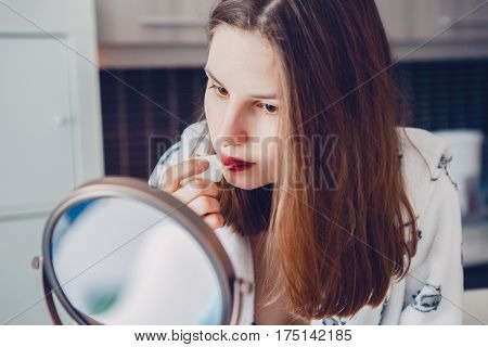Closeup portrait of young beautiful Caucasian white girl woman doing her makeup applying lipstick in front of the mirror in morning at home candid lifestyle natural light toned with filters