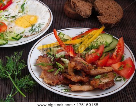 Fried bacon eggs and vegetables with pepper tomato and greens on white plates on a table on a bamboo napkin