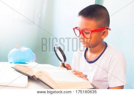 Little boy child wearing red glasses reading and using magnifying glass