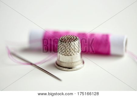 needlework and tailoring concept - thimble, sewing needle and thread spool