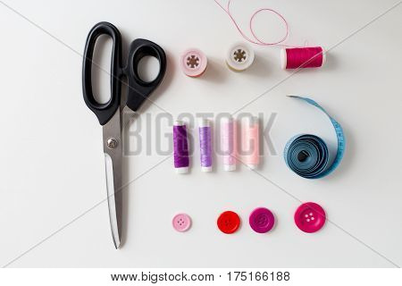 needlework and tailoring concept - scissors, sewing buttons, spools of thread and tape measure