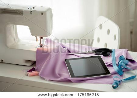 needlework, technology and tailoring concept - sewing machine with tablet pc computer, scissors, tape measure and fabric