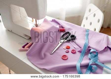 needlework, technology and tailoring concept - sewing machine with scissors, buttons, tape measure and fabric