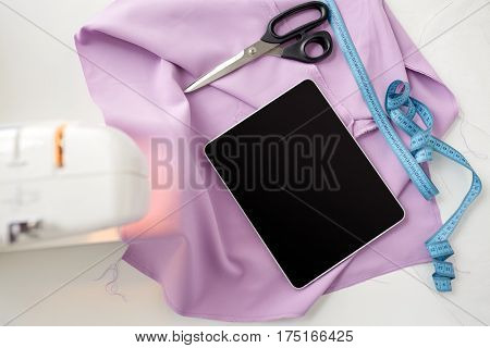 needlework, technology and tailoring concept - sewing machine with tablet pc computer, scissors, tape measure and fabric