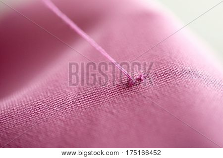 cross-stitch, needlework and tailoring concept - thread stitching on pink fabric