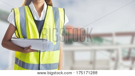 Mid section of female worker holding blue prints against construction site in background