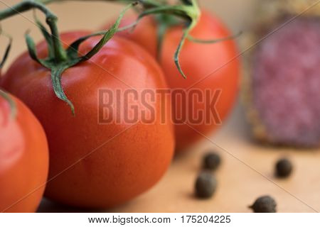 Detail of red tomatoes on a branch with delicious smoked sausage in background.