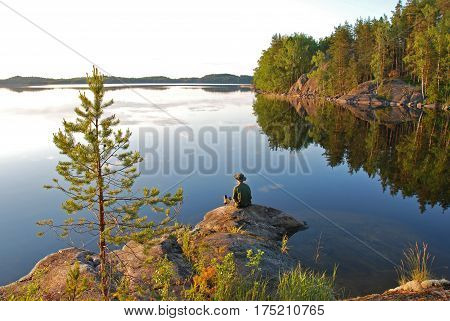 Man sitting at still Saimaa lake in Finland at sunset