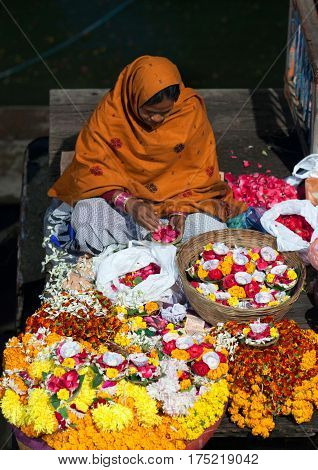 VARANASI, INDIA - JANUARY 3, 2016: Indian woman sitting on the ghats and selling pooja items for the offering - diya orange and yellow colored marigold flowers.