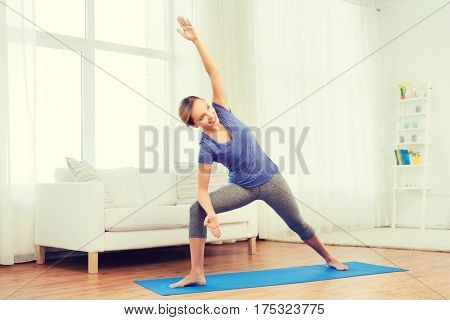 fitness, sport, people and healthy lifestyle concept - woman making yoga bikram triangle pose on mat