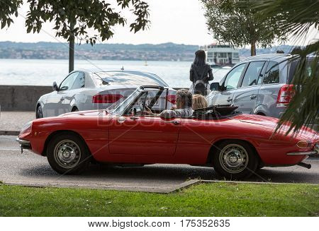 SIRMIONE ITALY - MAY 5 2016: Couple in vintage red cabriolet Alfa Romeo Giulietta Spider in Sirmione Garda Lake Italy