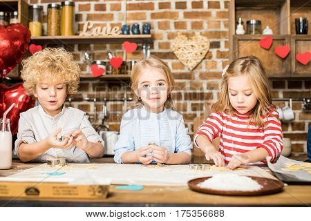 Three adorable little children cooking biscuits from unbaked dough