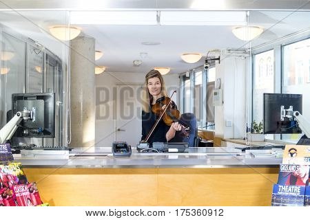 Friendly violinist behind a ticket counter selling tickets for a symphonic orchestra concert