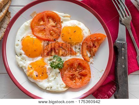 Delicious fried eggs with tomatoes served on white plate with red sides, old tableware, topview