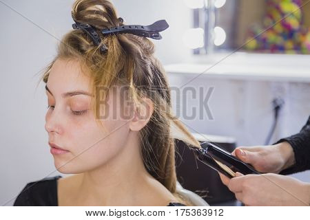 Hairstylist straightening the long brown hair of a female client using a heated hair straightener