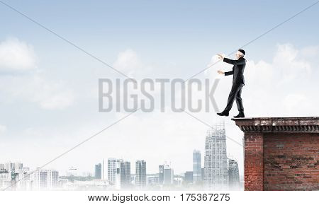 Businessman with blindfolder on eyes walking on building top