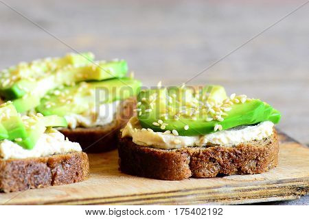 Open avocado and hummus sandwiches with sesame on a wooden board. Healthy vegan sandwiches. Closeup
