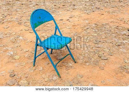 Old rusty foldable blue chair leave alone in abandoned dried backyard and fallen leaves on ground.