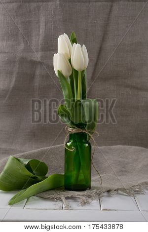 White tulips in green  glass bottle.Home interior decoration