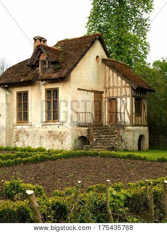 A traditional French cottage with a small garden and a thatched roof.