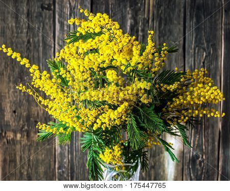 Beautiful bright bouquet of mimosa on a wooden background. Close-up. Spring bouquet with yellow flowers and green leaves.