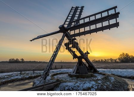 Tsjaker near Kalenberg during sunrise in wintertime with snow trees and ditch in National Park De Weerribben-Wieden in The Netherlands.