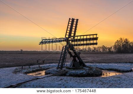 Tsjaker near Kalenberg during sunrise in wintertime with snow trees and ditch in National Park De Weerribben-Wieden in The Netherlands.