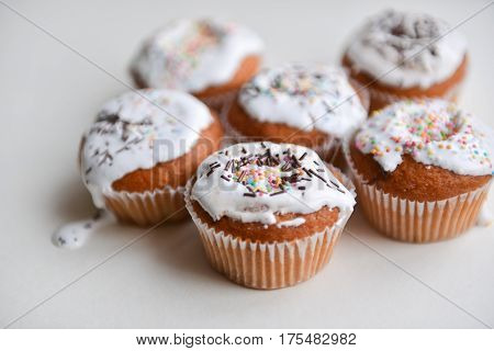 White authentic cupcakes made by hands with multicolored powder lying on white table