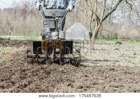 Tractor cultivating field at spring loosens soil by petrol cultivator close-up. Farmer working in the garden with garden tiller.