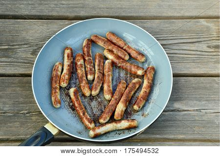 Grilled sausage cooked in pan on wooden background