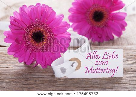 Label With German Text Alles Liebe Zum Muttertag Means Happy Mothers Day. Pink Spring Gerbera Blossom. Vintage, Rutic Or Aged Wooden Background. Card For Spring Greetings.