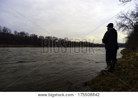 Early spring fisherman fishing off bank of fast flowing river at sunrise rugged outdoorsman